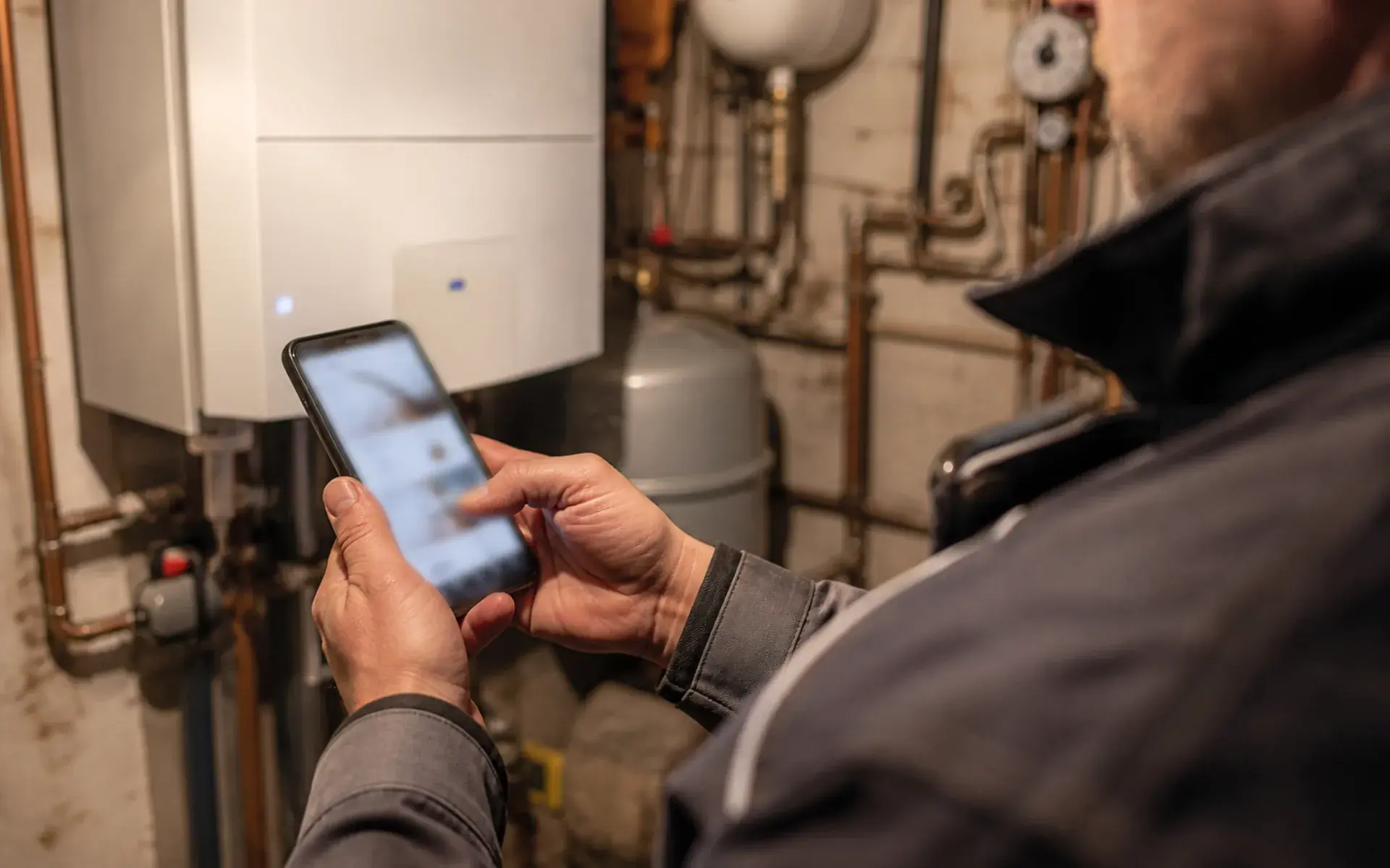 Monteur mit Handy im Heizungskeller